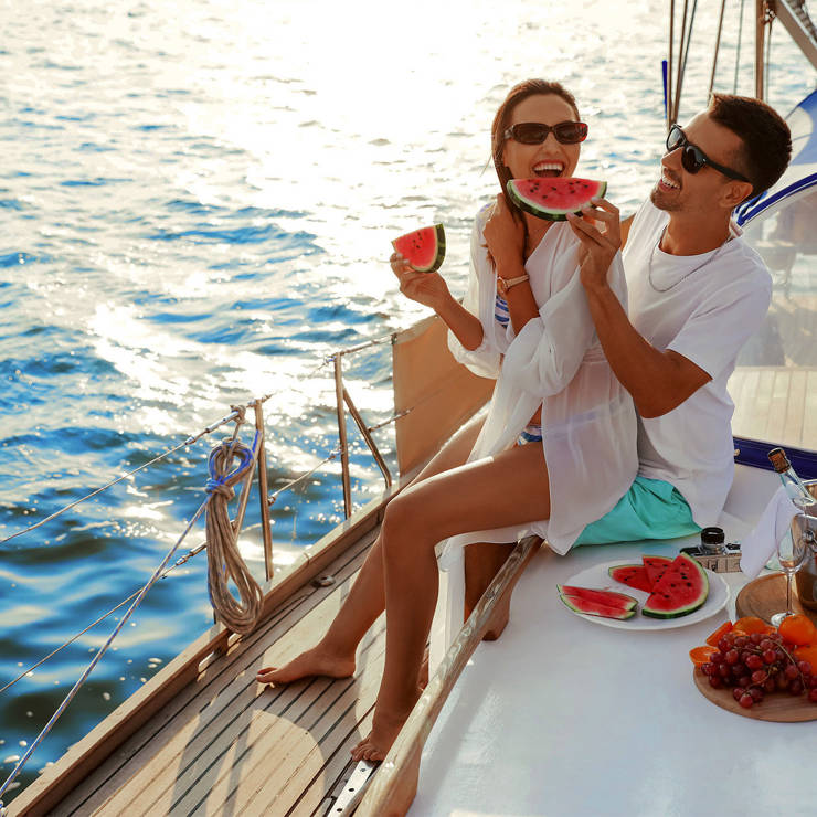 Couple relaxing on a yacht, on a private tour at sea, enjoying fresh watermelon and fruit with ocean views