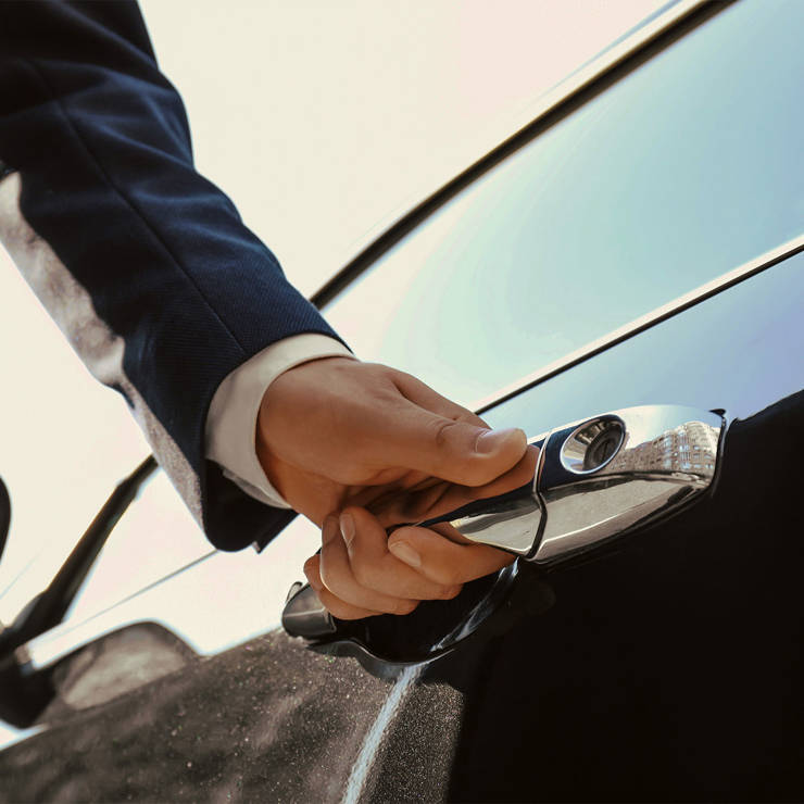 Person in a suit opening the door of a shiny black car, providing professional chauffeur or valet service