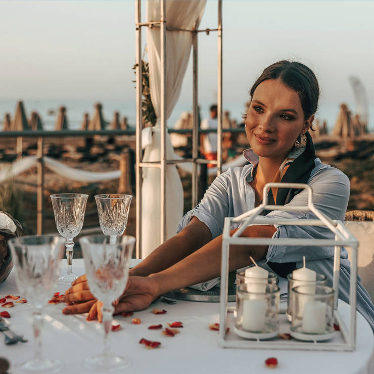 Woman enjoying romantic beachfront private dining at a table decorated with glasses, flowers, and candles