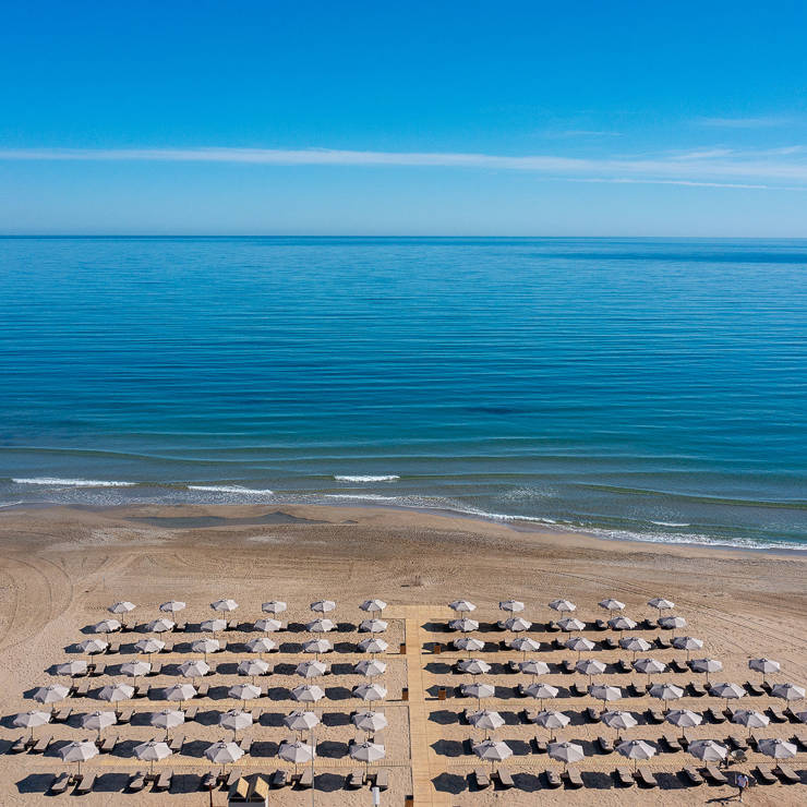 Wide beach view with rows of umbrellas and calm blue sea at Eliros Mare Hotel