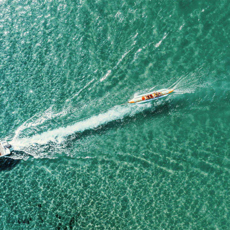Aerial view of speedboat pulling a banana boat with people across turquoise sea water