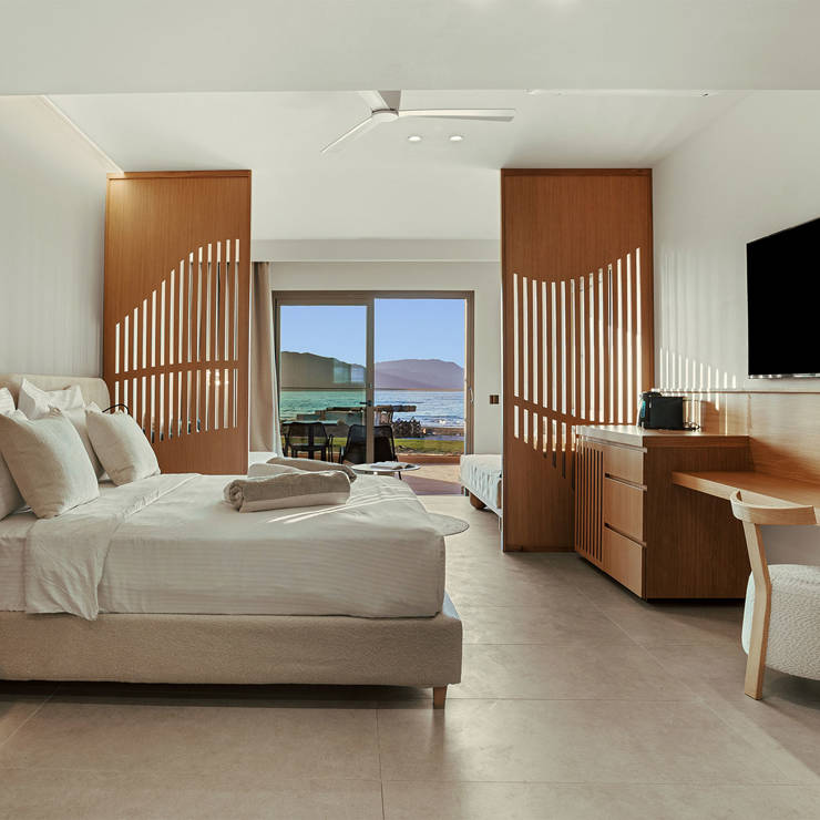 Elegant modern hotel room with wooden accents, king bed, work desk, and sea view terrace