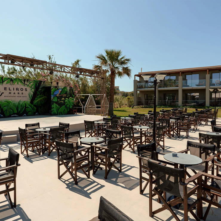 Outdoor entertainment stage and seating area at Eliros Mare Beachfront Resort, with tables and director's chairs facing a tropical-themed stage