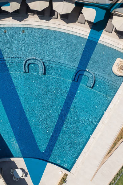 Large resort pool with sun loungers and umbrellas, geometric patterns in water, aerial view of Ventale Island Breeze Resort