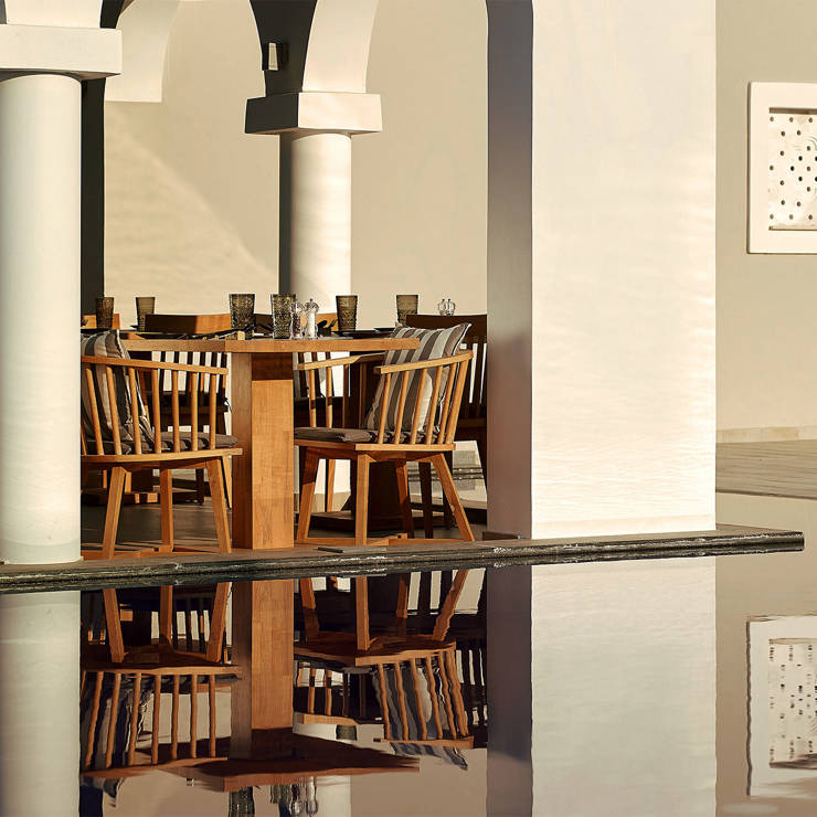 Outdoor restaurant seating with wooden tables and chairs under elegant white arches, reflected in a still pool