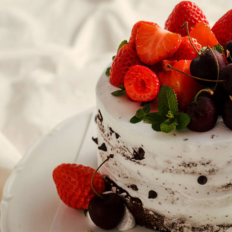 Naked cake with whipped cream frosting, topped with fresh strawberries, cherries, and mint leaves